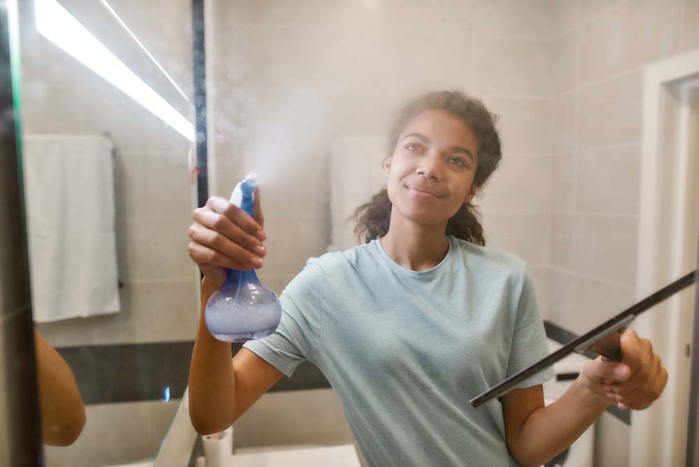 a young woman spraying a cleaning solution on a shower door to clean it